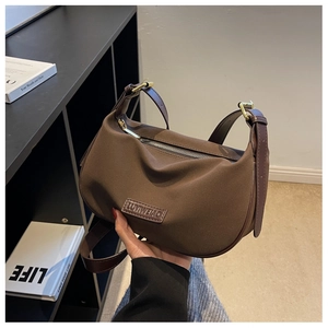 Detail of dark brown suede crescent bag with gold zipper and embossed brand logo