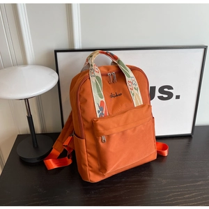 Détail d'un sac à dos orange avec broderie florale sur la sangle et poche latérale pratique