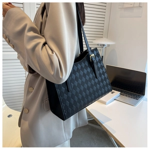 Detail of black quilted tote bag with gold buckle on shoulder strap and leather texture