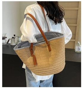 Detail of hand-woven straw tote with leather straps, tassels, and striped fabric lining