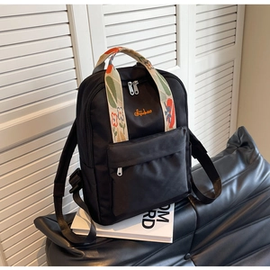 Détail d'un sac à dos noir avec broderie florale colorée sur la poignée de transport