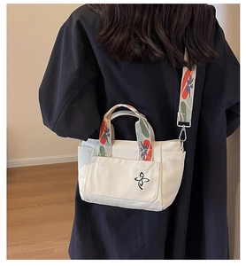 Detail of white canvas tote bag featuring embroidered logo and colorful floral woven strap