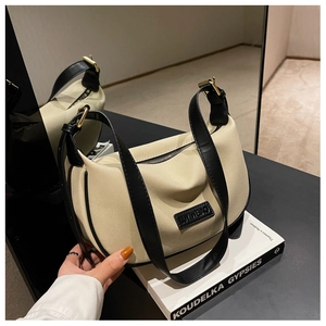 Detail of cream crossbody bag featuring black leather trim and embossed brand logo