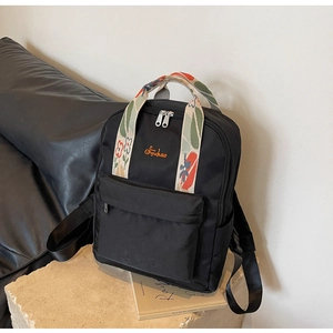 Détail d'un sac à dos vintage noir avec des sangles brodées fleuries et poche avant