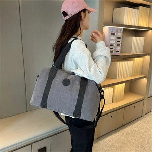 Large dark grey travel bag with shoulder strap and handles against a cozy bookshelf background