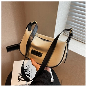 Detail of beige shoulder bag with black strap, gold hardware and textured finish