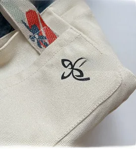 Detail of canvas tote bag with black logo embroidery and colorful patterned strap
