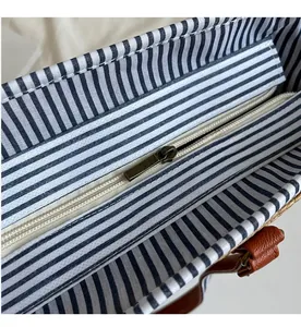 Detail of smooth brass zipper and blue striped lining of a straw tote bag