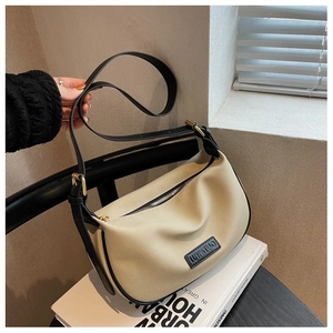 Detail of a beige canvas shoulder bag with black trim and brand leather logo
