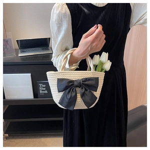 Dettaglio della borsa a secchiello intrecciata beige con grande fiocco di raso nero