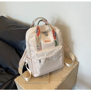 Détail du sac à dos beige avec broderie florale et fermetures éclair doubles en métal
