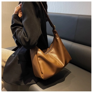 Detail of a brown PU leather hobo bag with natural folds shown on a modern sofa