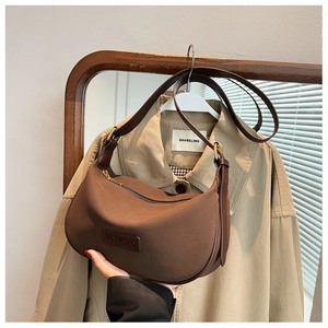 Detail of dark brown leather crescent bag with brand logo and adjustable shoulder strap