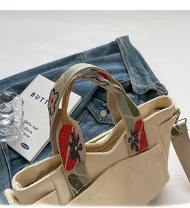 Detail of floral embroidery on wide strap of a beige canvas tote bag with shoulder strap