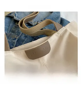 Detail of off-white canvas tote bag with brown leather handles and stitched logo patch