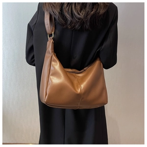 Detail of a dark brown faux leather hobo bag worn by a model in a black blazer suit
