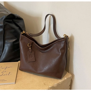 Detail of a dark brown leather tote bag featuring gold hardware and a brand logo tag