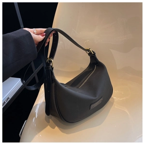 Detail of minimalist black hobo bag with adjustable strap and matte finish on a soft chair