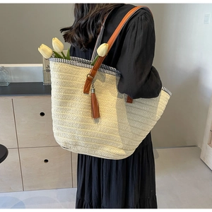 Detail of handwoven straw tote bag with brown leather handles and a decorative tassel