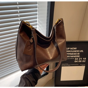 Detail of dark brown leather tote bag featuring gold hardware and logo hangtag pendant