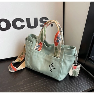 Detail of green canvas tote with embroidered flower and colorful patterned strap