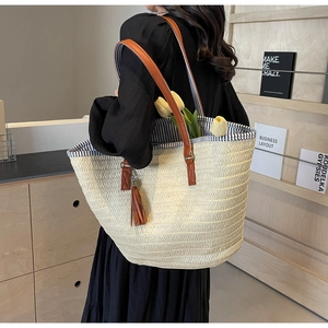 Detail of straw tote bag with brown leather straps, tassel charm and striped lining
