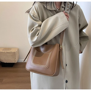 Brown leather bucket bag with white contrast stitching and geometric woven shoulder strap