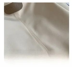 Close-up of cream canvas tote bag with brown leather logo patch and double stitching