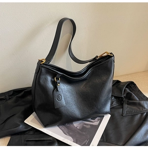 Detail of the black vintage textured crossbody bag with a round logo tag and gold hardware