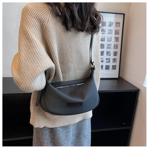 Detail view of the black half-moon crossbody bag with leather logo patch on beige sweater