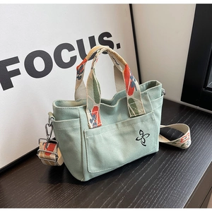 Detailed macro of green canvas tote bag showing floral strap and butterfly logo
