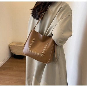 Detail of caramel leather bucket bag with white contrast stitching and wide shoulder strap