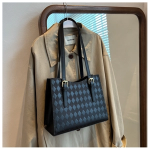 Detail of black quilted tote bag with golden hardware on a classy trench coat backdrop