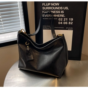 Detailed close-up of a large black leather hobo bag with vintage gold buckle and round logo tag