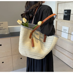 Close-up of beige woven straw tote bag with brown leather straps and long tassel detail