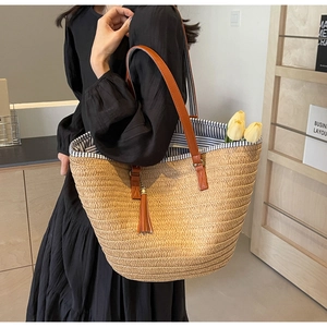 Detail of straw tote bag showing brown leather handles and decorative tassel ornament