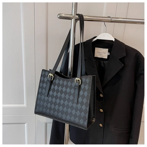 Close-up of black quilted tote bag with smooth PU leather and gold-toned metal buckles