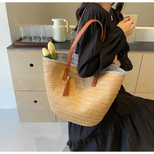 Detail of a large straw tote bag featuring brown leather straps and striped lining interior