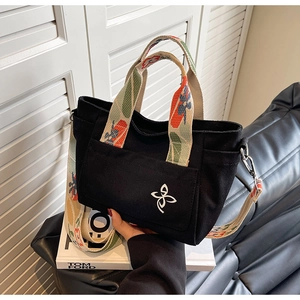 Detail of black canvas tote bag showing colorful patterned strap and embroidered floral logo