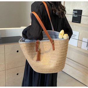 Close-up of woven straw tote bag featuring blue striped lining and brown leather straps