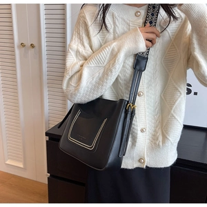 Detail of black leather bucket bag featuring metal U-shape studs and woven wide strap