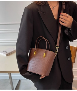 Close-up of brown crocodile texture bucket bag with golden hardware on black blazer