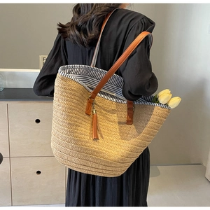 Close-up of straw tote bag showing brown leather straps and blue striped lining