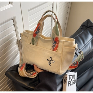 Detail of canvas tote bag with floral logo and colorful bohemian woven strap on leather seat