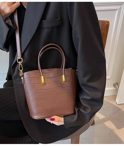 Close-up of brown crocodile embossed leather texture and gold hardware on bucket bag