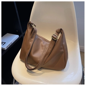 Brown faux leather crescent bag with adjustable wide strap shown on a chair
