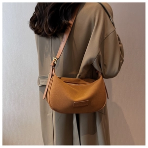 Brown suede dumpling bag shown on shoulder of a model wearing a long trench coat