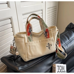 Detail of off-white canvas tote bag featuring colorful floral strap and butterfly embroidery