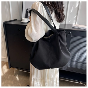 Detail of black canvas tote bag with leather straps and rivet reinforcements on model
