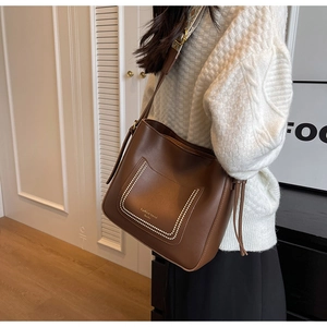 Detail of dark brown leather bucket bag with white stitching and retro geometric wide strap